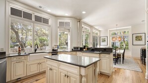 A spacious kitchen with large windows, a central island, and a dining area with a chandelier. - Pristine 2nd row home in Sea Pines w/ great outdoor space, private pool & spa (Hilton Head Island)