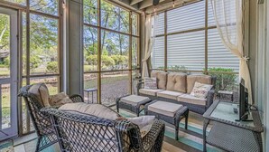 A sunroom with wicker furniture, a sofa, and a television.