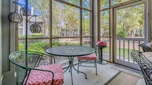 A covered patio with a round table and chairs, large windows, and a grill.