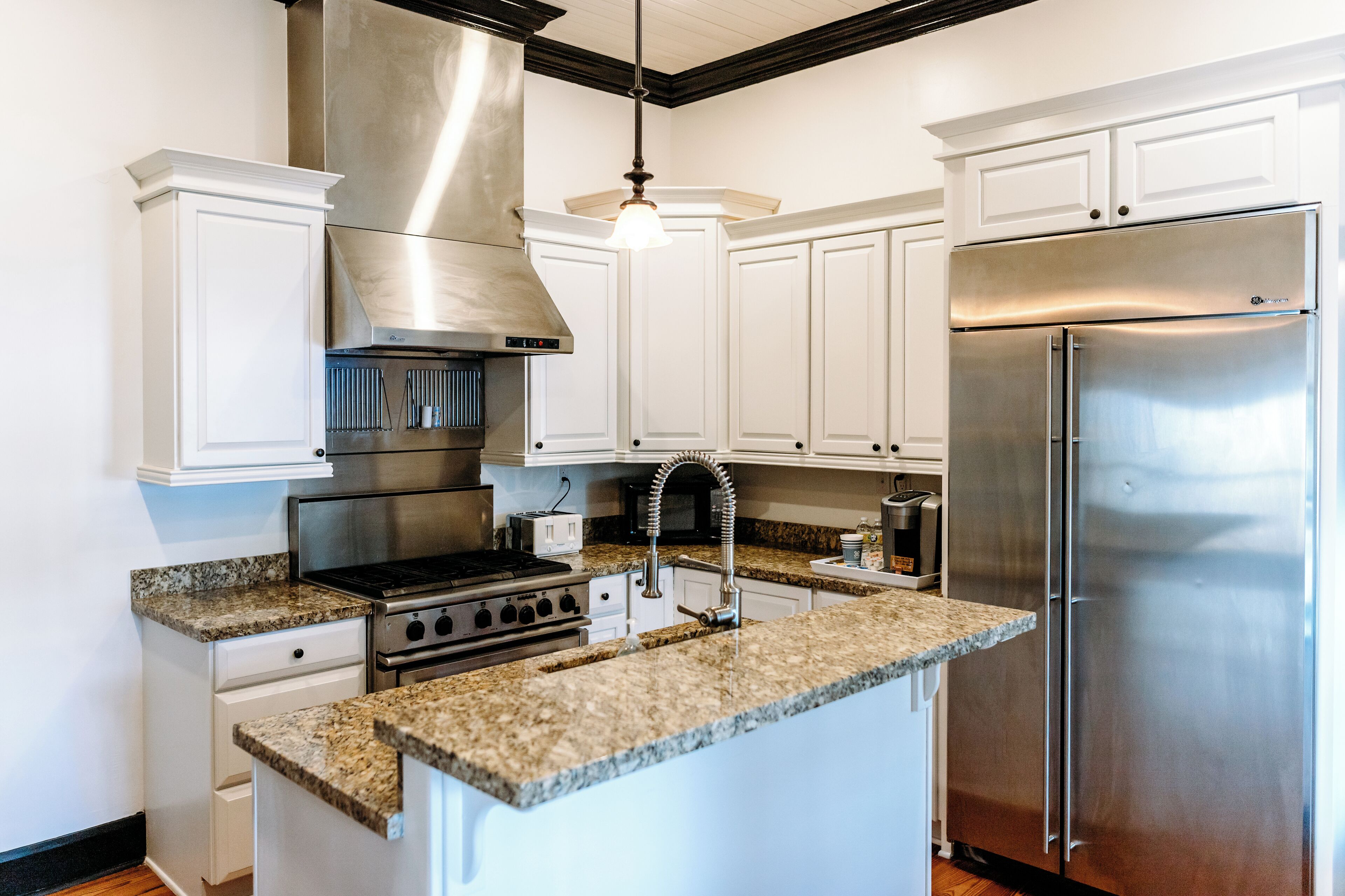A kitchen with white cabinets, a stainless steel range hood, a double-door refrigerator, granite countertops, and a stainless steel sink.