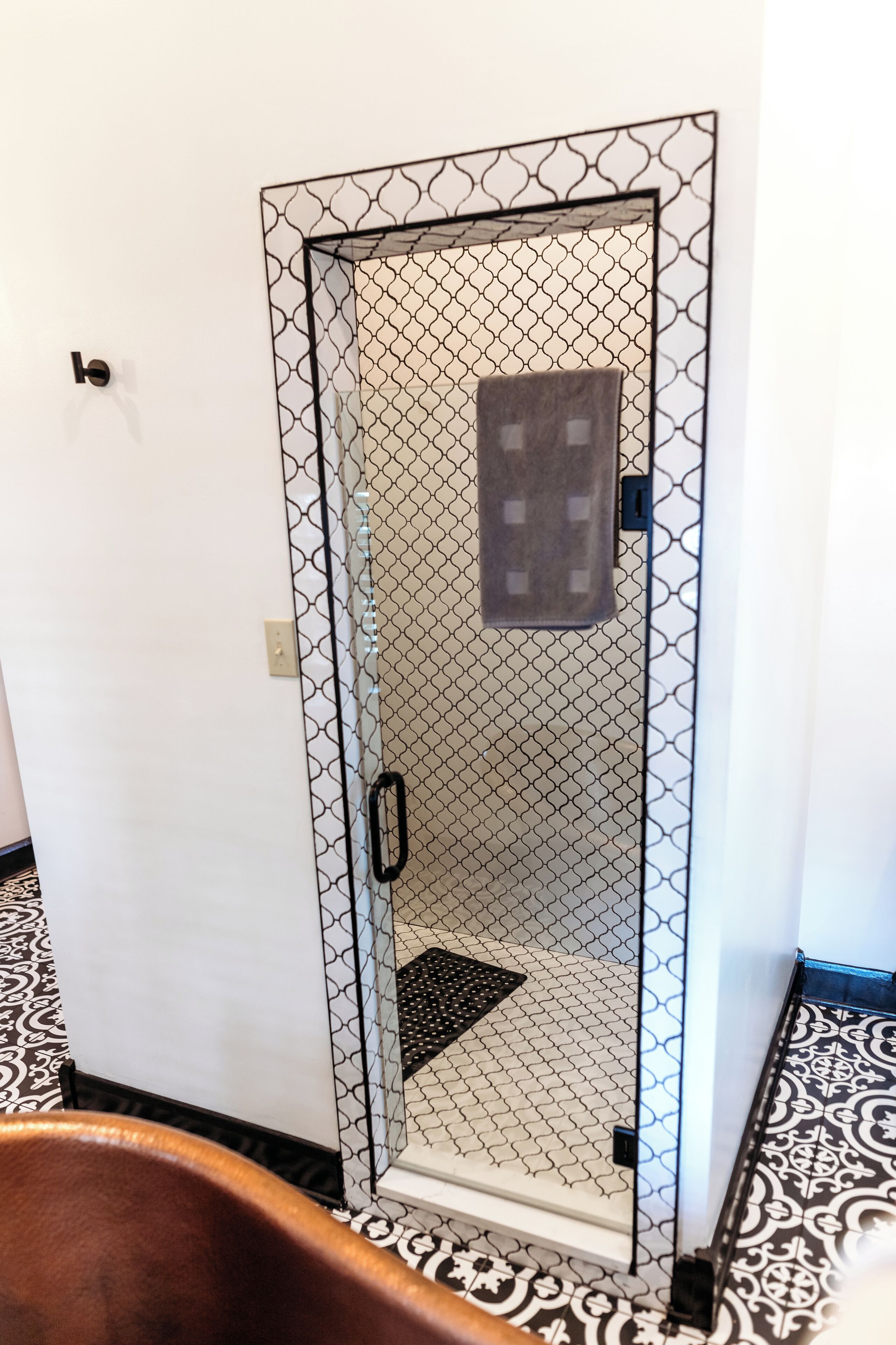 Zona de ducha con vidrio, suelo estampado y un perchero.