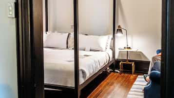 A four-poster bed in a room with wooden flooring, a bedside table with a lamp, and a striped rug.