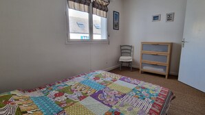 Ein Schlafzimmer mit einer farbenfrohen Stegdecke, einem Stuhl, einem Holzregal und einem Fenster mit Vorhängen.