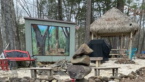 Ein Steinstapel in einer natürlichen Umgebung mit einer Holzkonstruktion und einem Gemälde im Hintergrund.