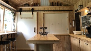 Ein Holzeinrichtung mit einem zentralen Tisch, Barhocker, einer Pendelleuchte und einem Fenster mit Vorhang.