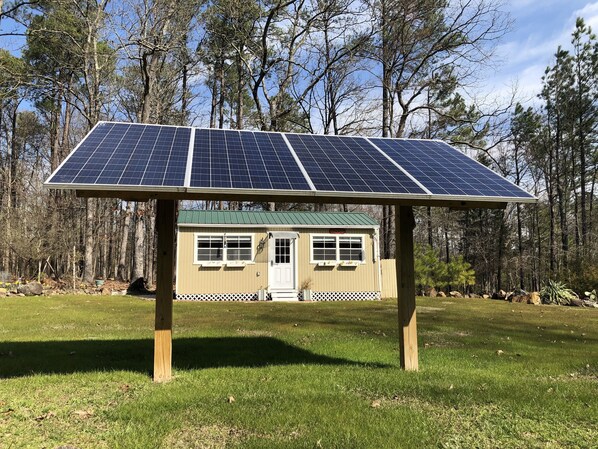 Una casa pequeña con un panel solar en el techo, rodeada de un bosque.