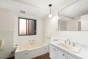 Een badkamer met een bad, een wastafel, een spiegel en een raam.