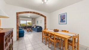 A spacious living area with a dining table, blue sofa, and a view through an archway to a balcony.