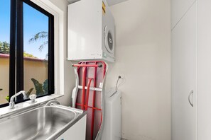 A compact kitchen with a stainless steel sink, a window, and a white wall-mounted fan.