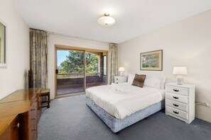Een hotelkamer met een groot bed, een klein nachtkastje, een raam met gordijnen, een schilderij aan de muur en uitzicht op groen.