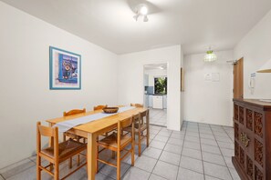 Een eetruimte met een houten tafel en stoelen, een inlijsting foto aan de muur en een keuken op de achtergrond.