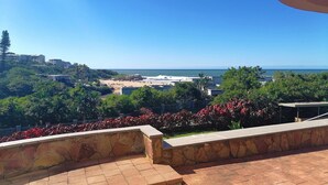 A coastal view with a stone pathway leading to a seating area overlooking the beach and ocean. - Claridges 104 (Margate)