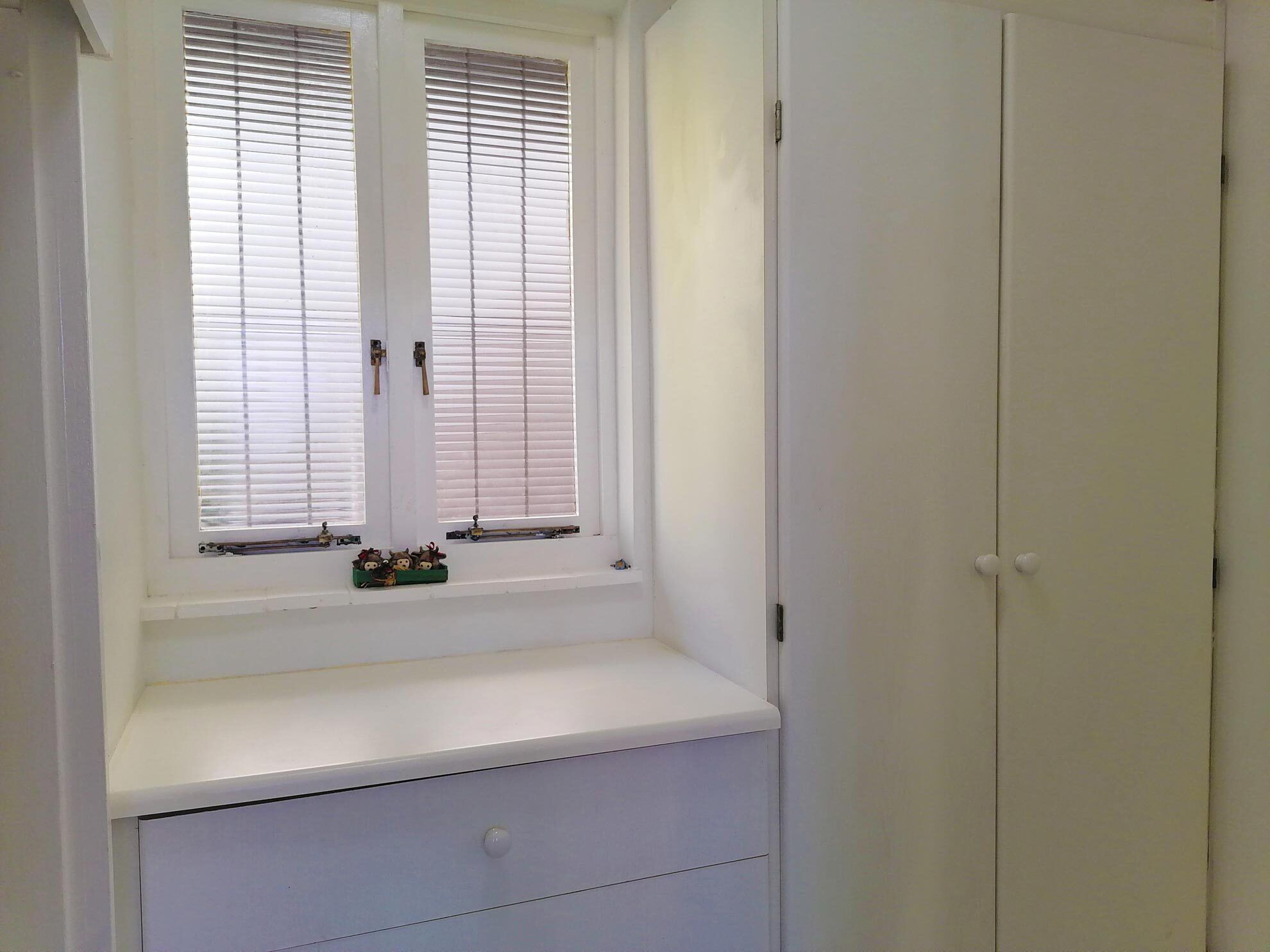A white room with a window, a white door, and a white cabinet.