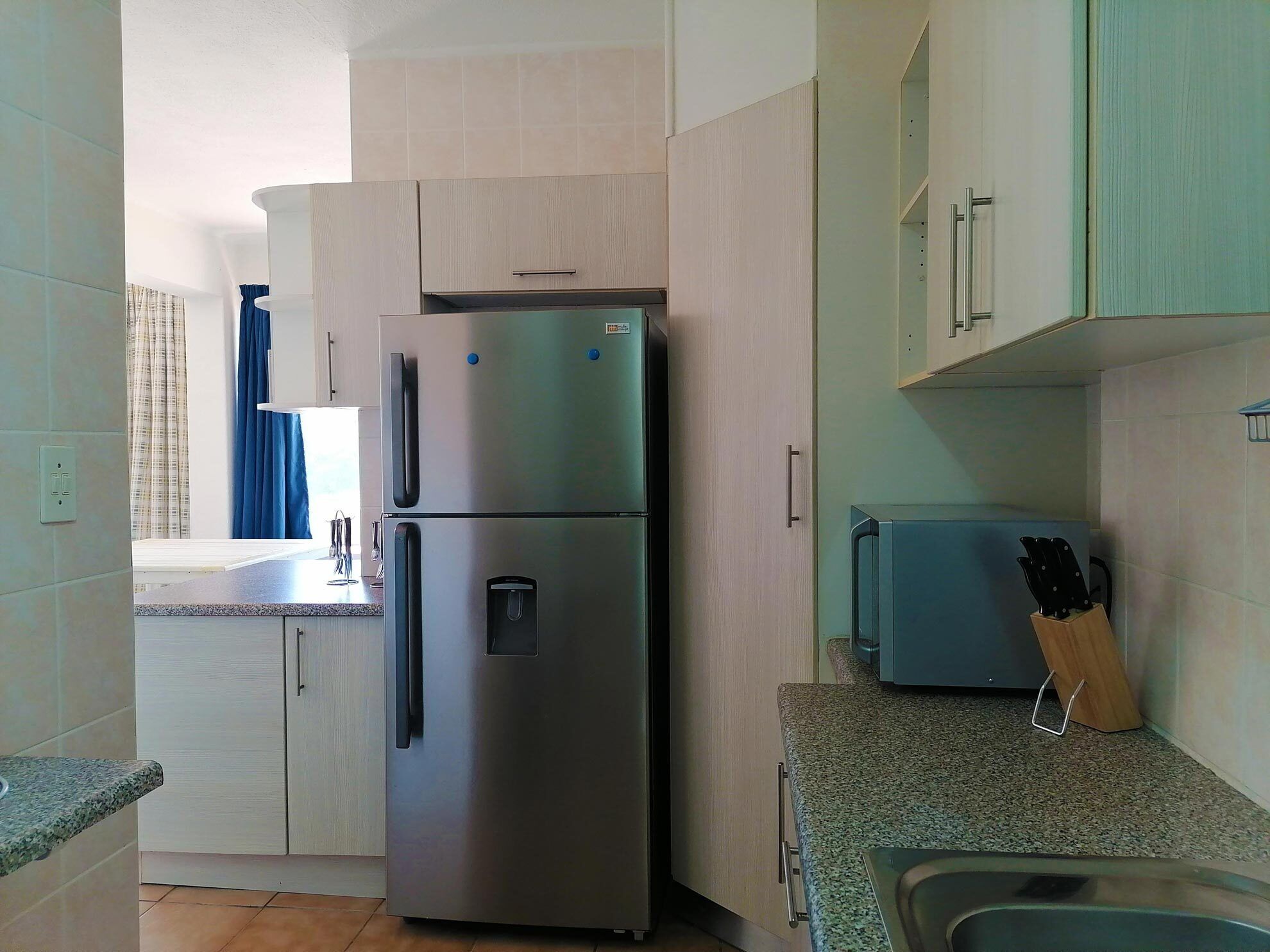 Cocina compacta con refrigerador de acero inoxidable, microondas integrado y un lavamanos.
