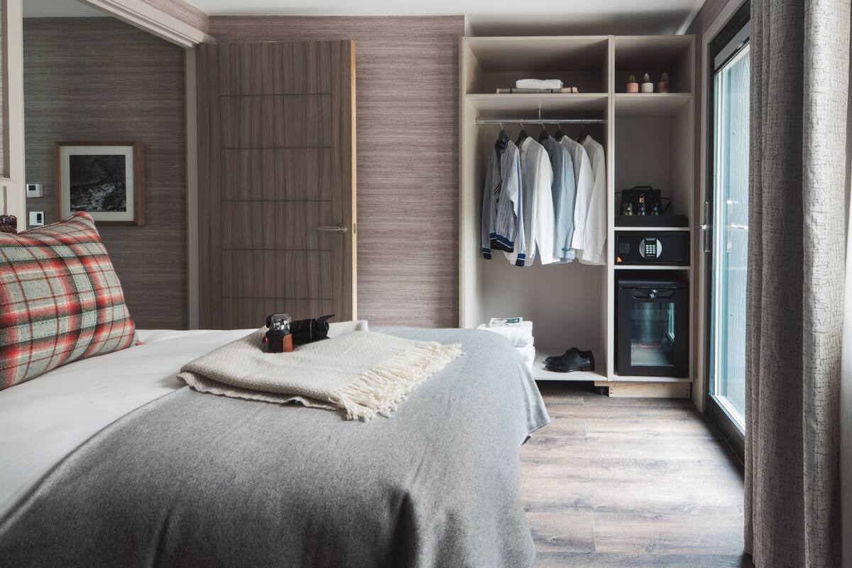 A bedroom with a bed, a wardrobe, a closet with hanging clothes, and a window.