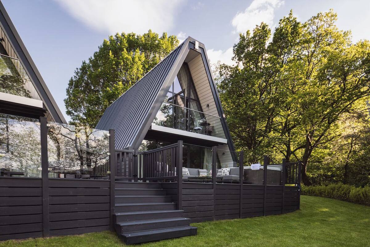 A modern outdoor deck with a sloped roof, built into a wooden structure, surrounded by lush greenery.
