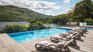 A poolside area with lounge chairs and a view of a lake and hills. - Ardlui Retreat (Arrochar)