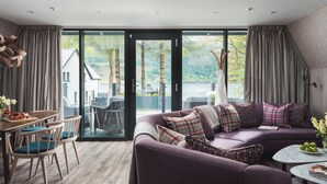 A modern living room with a purple sofa, a dining area with wooden chairs, and a large glass door leading to a scenic outdoor view. - Ardlui Retreat (Arrochar)