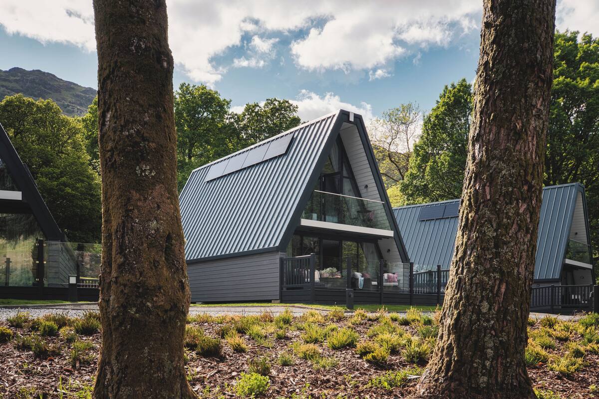 A modern house with a sloped roof, surrounded by trees and a mountainous backdrop.