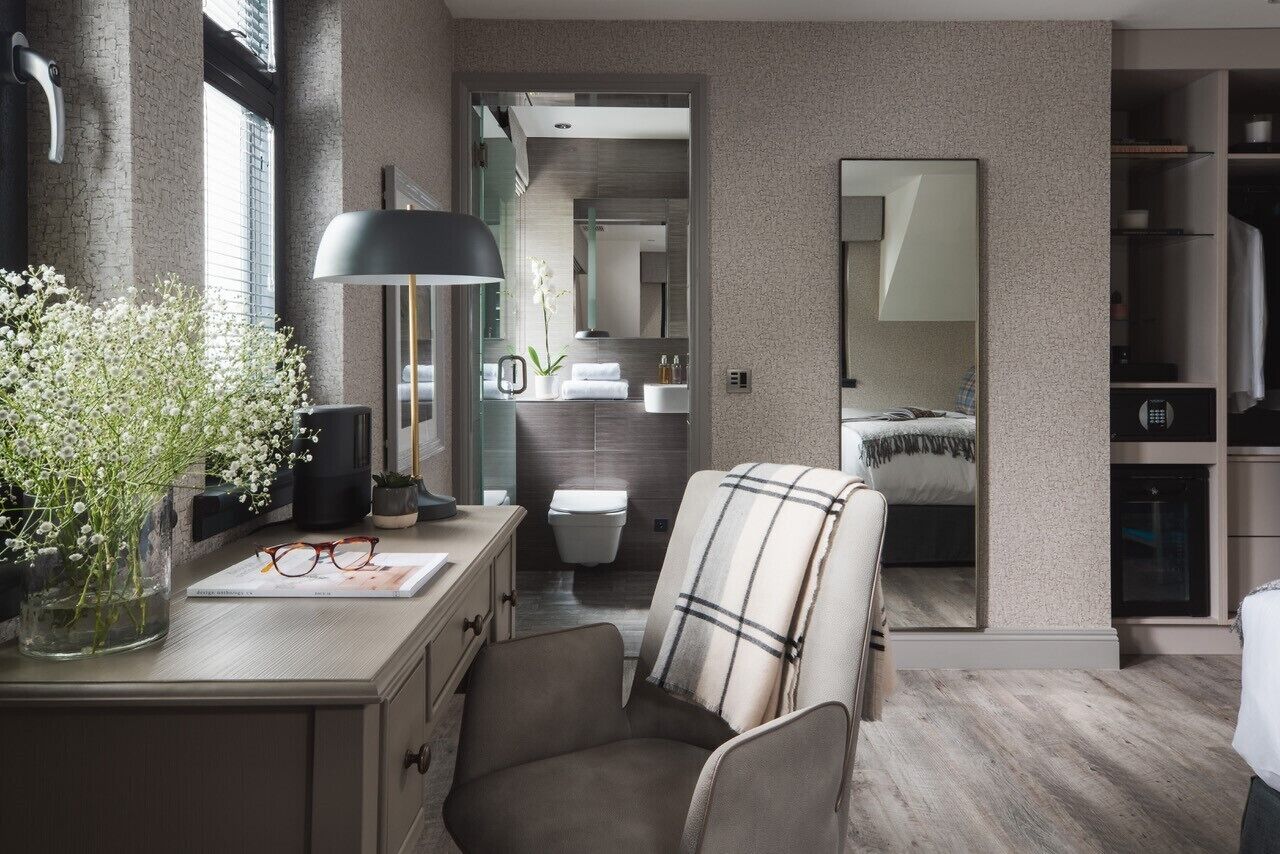 Une chambre moderne avec un grand miroir, une table de chevet, une chaise et une vue sur la salle de bain.