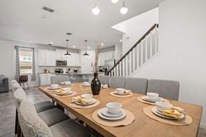 Uma cozinha moderna com armários brancos, uma mesa de jantar de madeira posta com pratos, tigelas e um vaso.