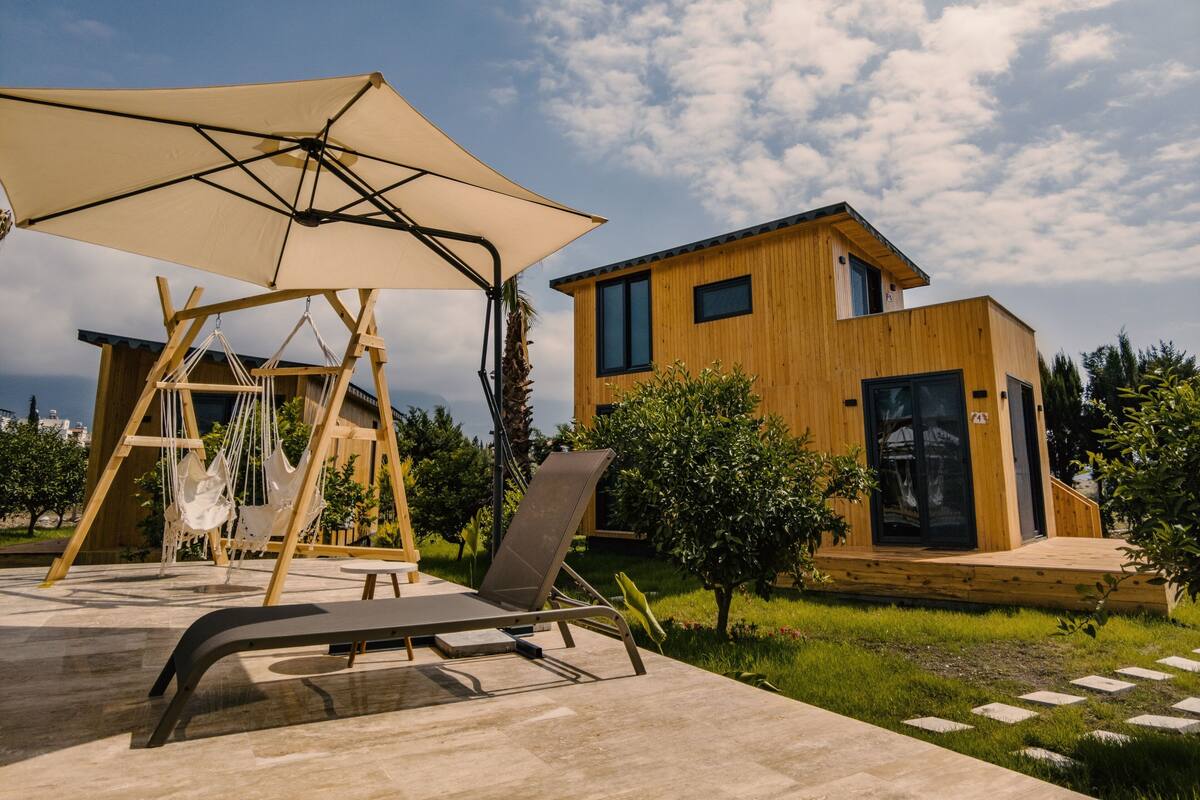 Een modern houten huis met een balkon, een hangmat en een lounge stoel onder een grote parasol.