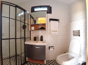 A modern bathroom with a glass shower enclosure, a sink with a mirror above, a toilet, and a towel hanging on the wall. - Arsuz Bungalov (Arsuz)
