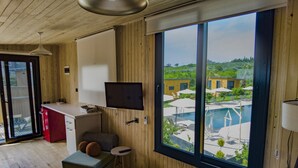 A modern room with a large sliding glass door to a pool area, a small kitchenette, a bed, and a TV mounted on the wall. - Arsuz Bungalov (Arsuz)