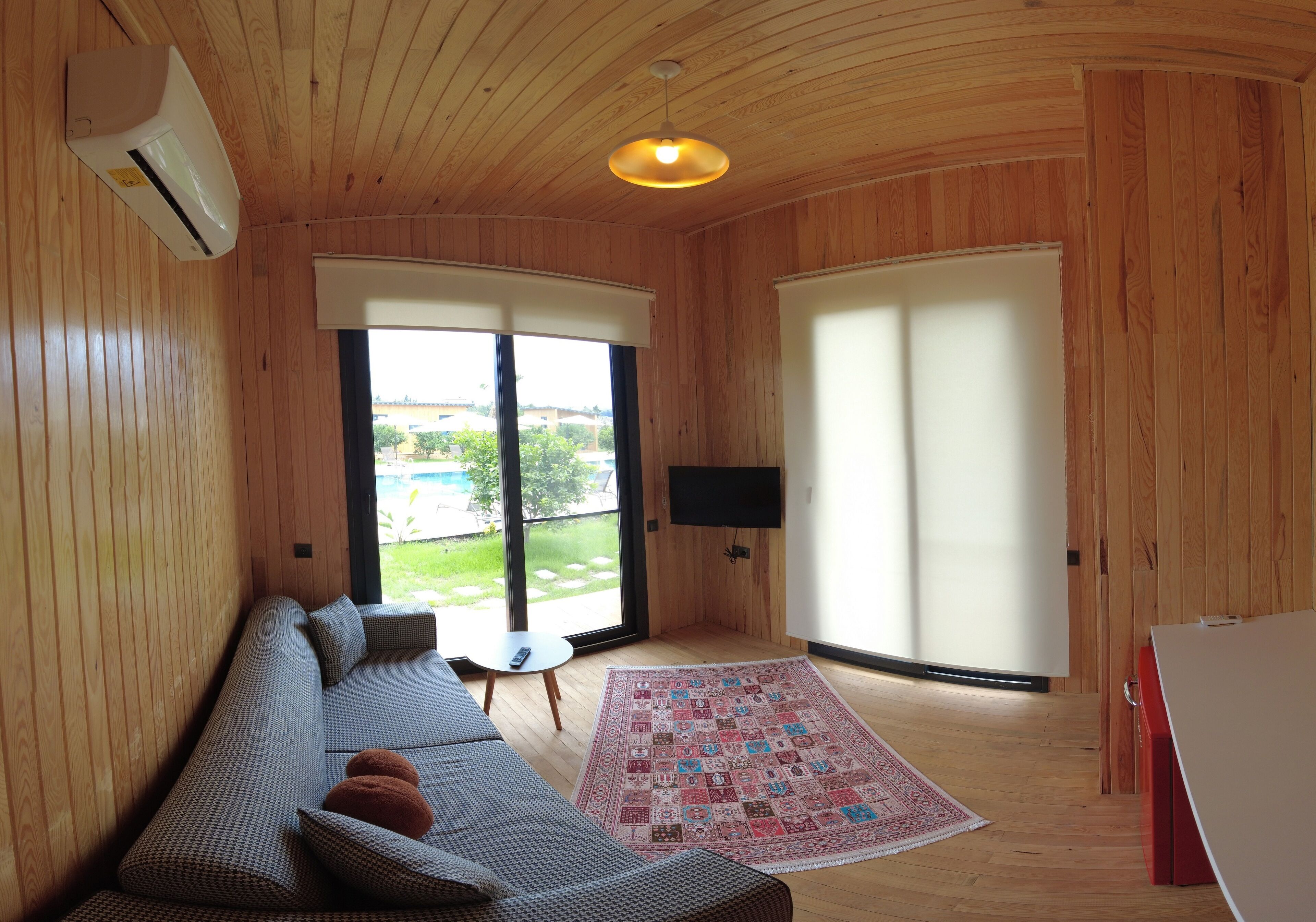 Une pièce avec un plafond en bois, une grande fenêtre, un canapé, un téléviseur et un tapis.