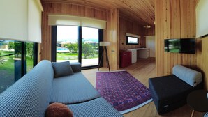 A modern interior with a wooden ceiling, a sofa, a rug, and a TV in a room with large windows. - Arsuz Bungalov (Arsuz)