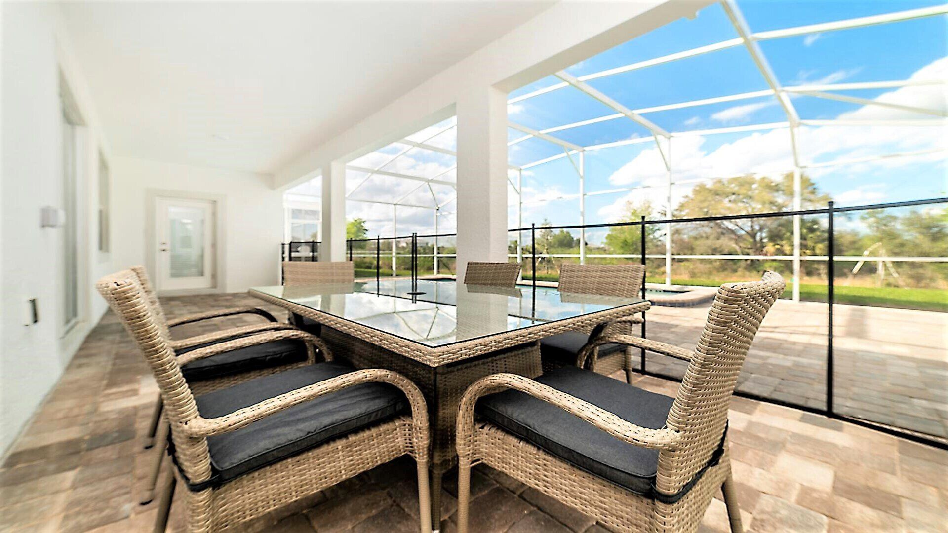 Un espace repas entièrement vitré, avec une table en verre et des chaises en osier.