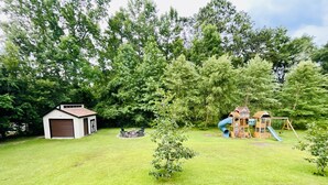A backyard with a wooden playhouse, a small shed, and a well-maintained lawn. - Lovely Guest Apartment<br> (Pace)