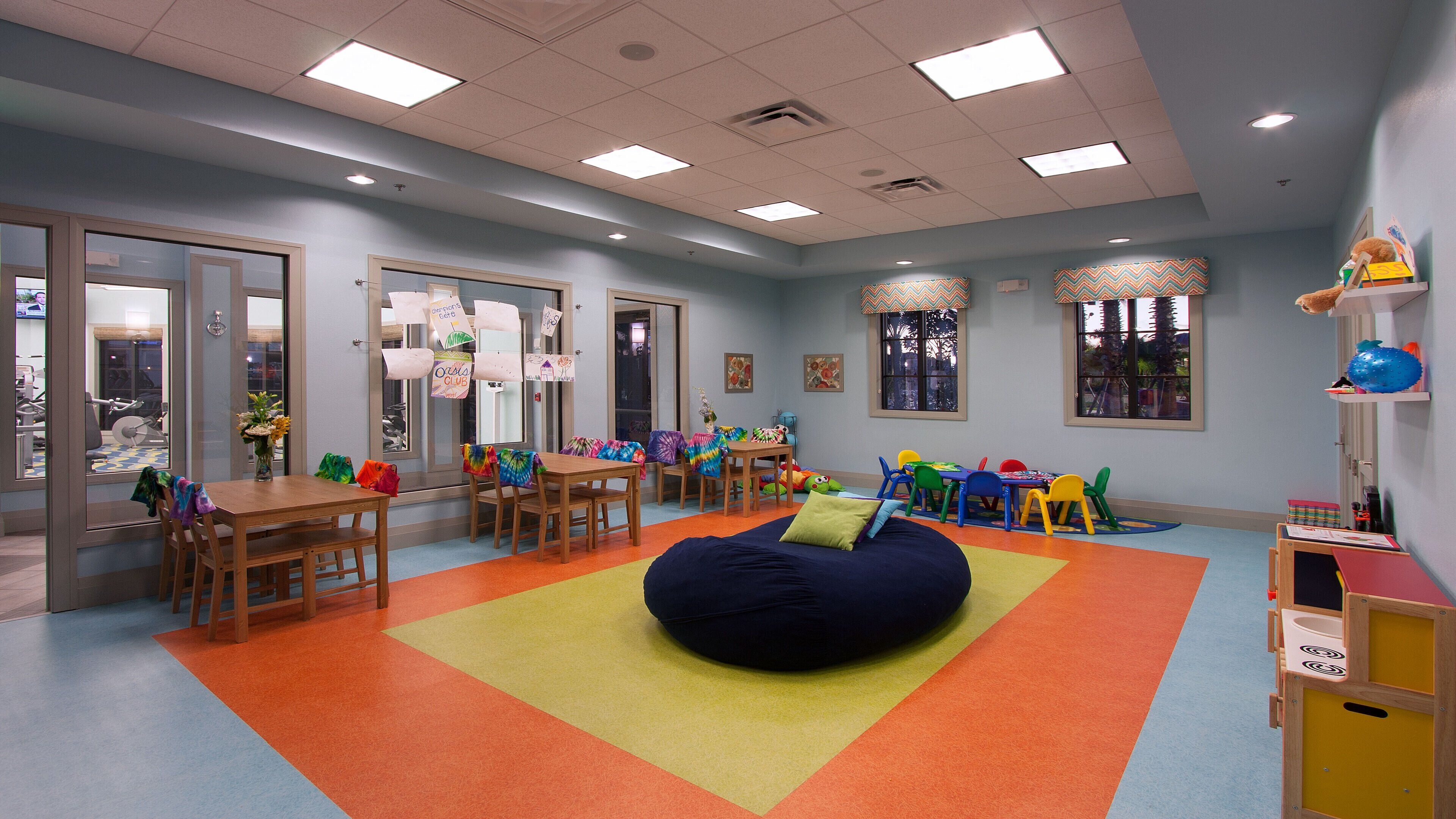 Ein helles Kinderzimmer mit Tischen, Stühlen und Sitzsack.