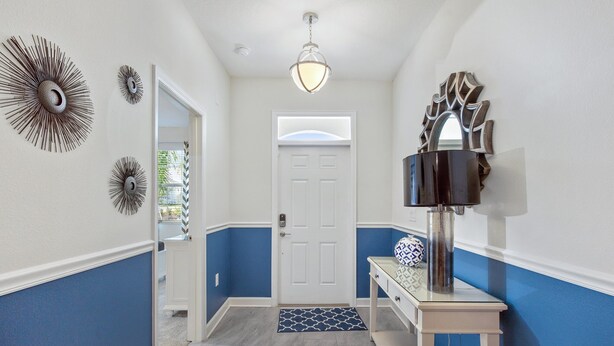 Un couloir avec une porte blanche, des murs bleus, un tapis à motifs et une table sur laquelle est posé un objet décoratif.