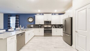 Kitchen features a central island with a sink, stainless steel refrigerator, and microwave above the oven.