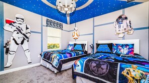 Quarto com roupa de cama temática de Star Wars, teto com desenho de estrelas e uma figura de Stormtrooper.