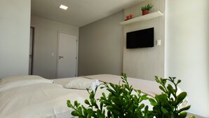 A bedroom with two beds, a TV mounted on the wall, and a door. - Pé na Areia, Vista Mar e 3 Qts com AC (Barra de São Miguel)
