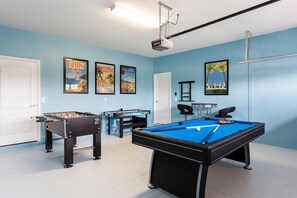 A room with a pool table, foosball table, and two framed posters on the wall.