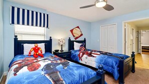 Un dormitorio con dos camas, cada una con una colcha de superhéroes, un ventilador de techo y decoración de pared con temática de béisbol.