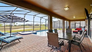 Uma área externa coberta com piscina, espreguiçadeiras e uma mesa de jantar.