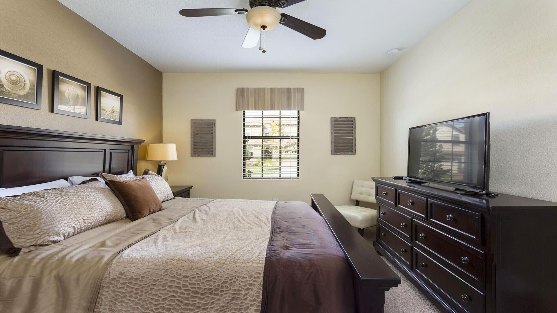 A hotel room with a bed, a TV, a dresser, and a ceiling fan.