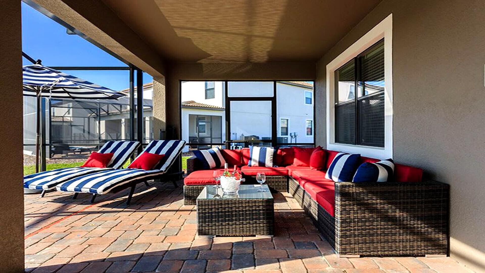 An outdoor patio with wicker furniture, a glass table, and red cushions.