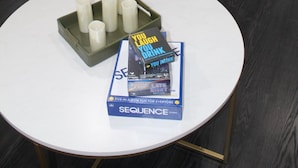 Une pièce avec une table ronde blanche, un plateau avec des bougies et un livre intitulé « Vous buvez, vous mourez, vous buvez ».
