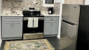 Une cuisine avec des meubles de couleur grise, un réfrigérateur noir, une cuisinière en acier inoxydable et un tapis à motifs.