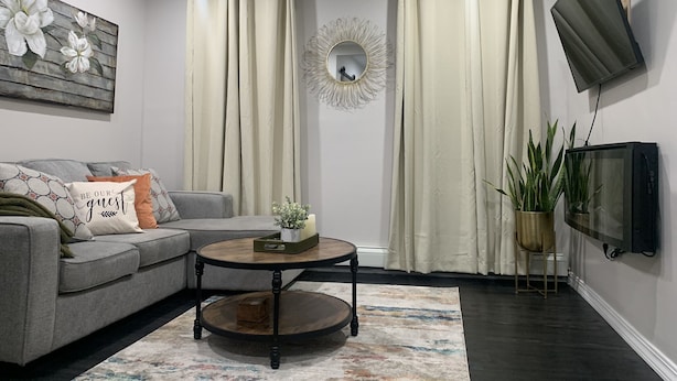 Un salon avec un canapé gris, une table basse, un téléviseur à écran plat fixé au mur et un miroir décoratif.