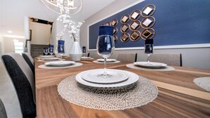 Un coin repas avec une longue table en bois dressée pour le repas, agrémentée de sets de table en fibres tressées et de verres transparents.