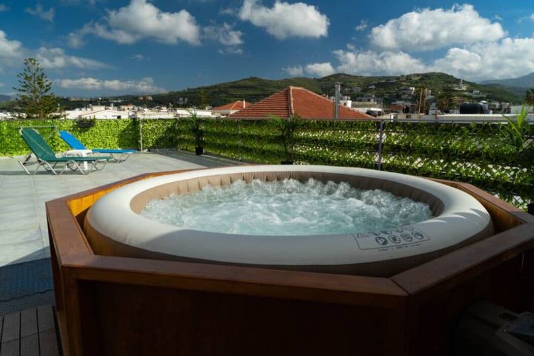 Un bain à remous entouré de chaises longues sur une terrasse offrant une vue sur la ville et les collines.