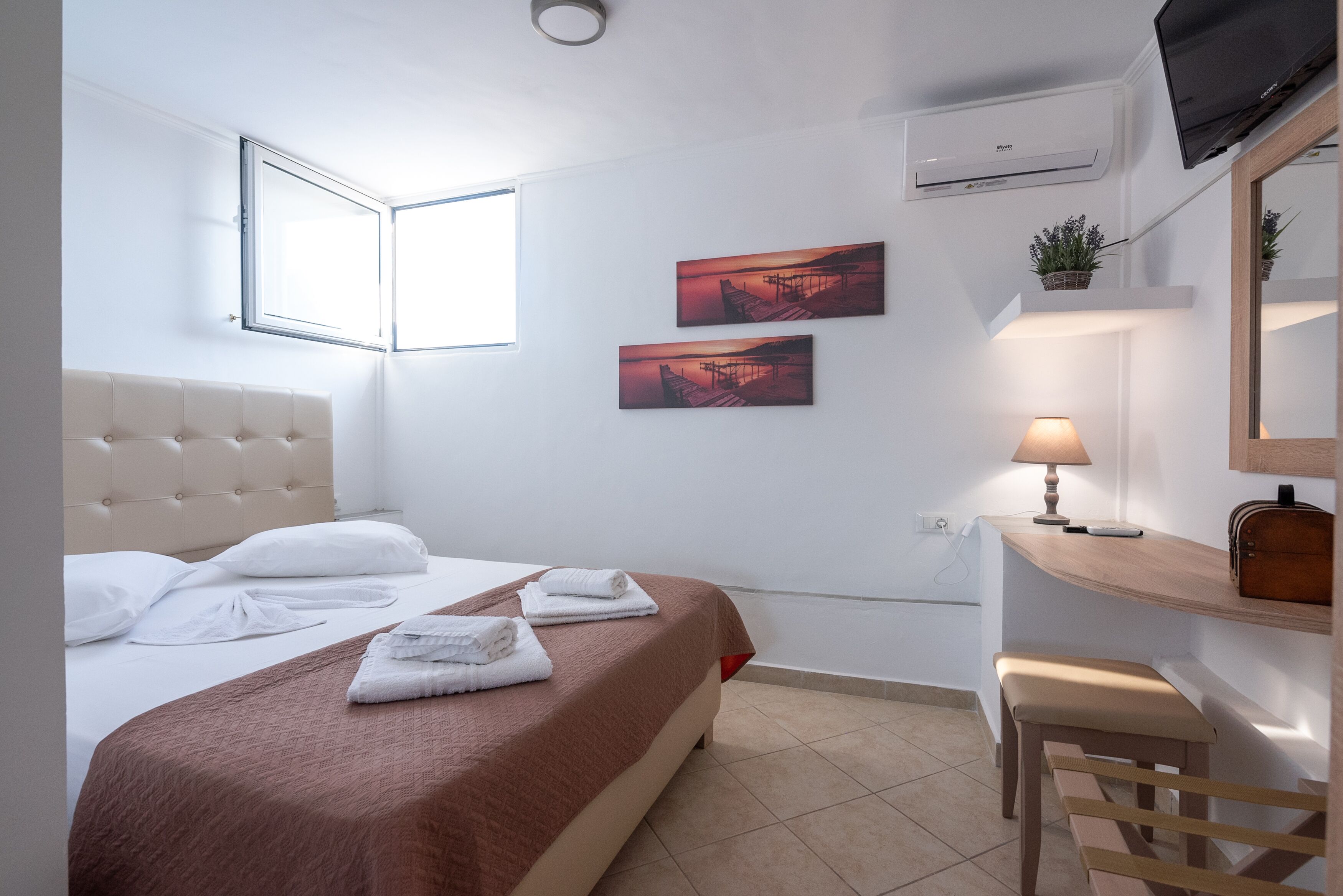 A hotel room with a bed, a desk, a chair, a TV, and two paintings on the wall.