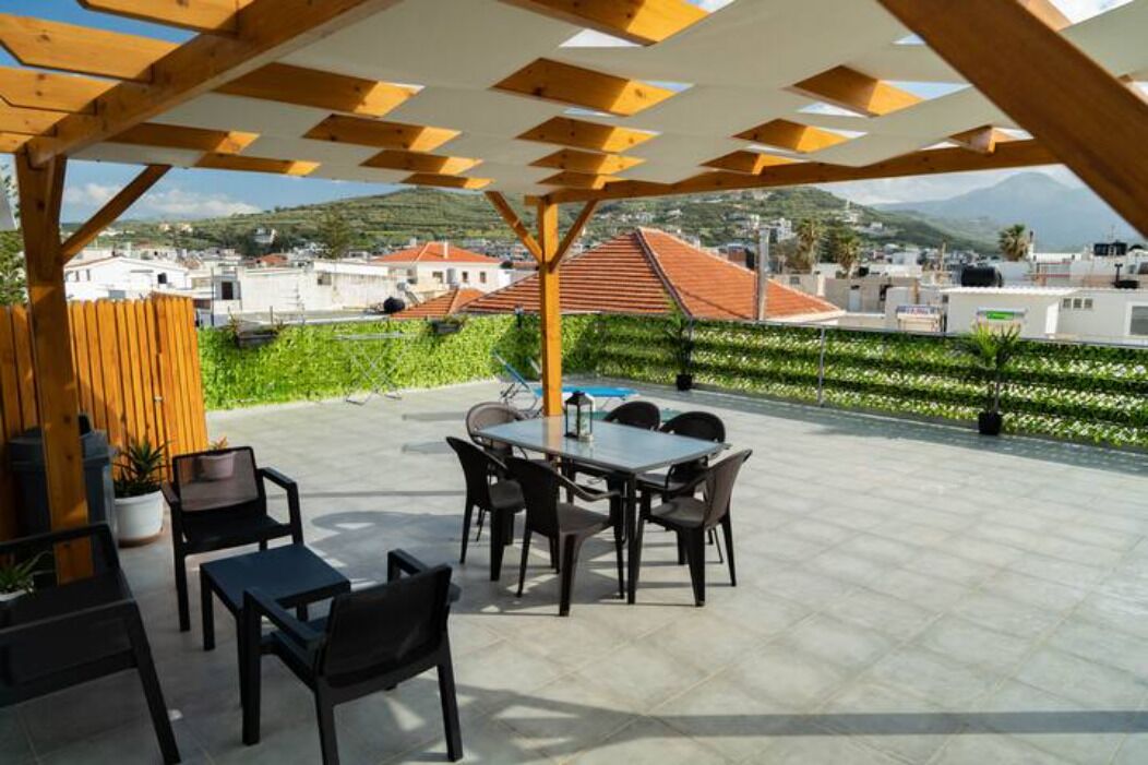 Une terrasse extérieure avec une table et des chaises, entourée de verdure et offrant une vue sur des bâtiments et des montagnes.