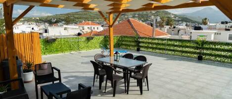 Une terrasse extérieure avec une table et des chaises, entourée de verdure et offrant une vue sur des bâtiments et des montagnes.